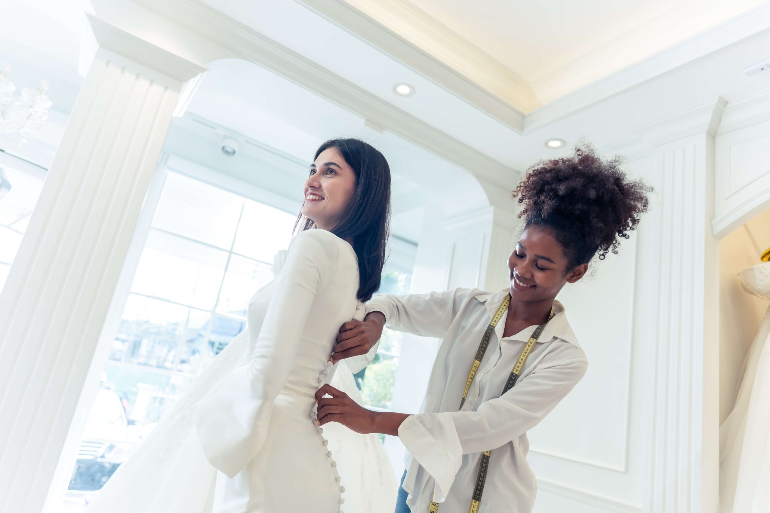 woman in wedding dress while tailor measures her for fitting