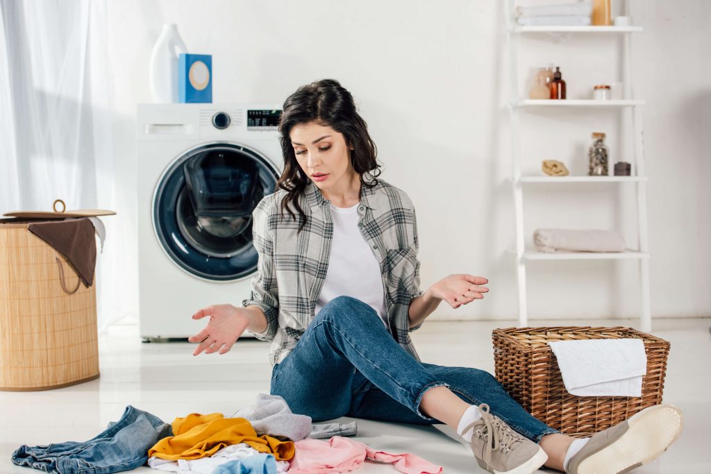 woman confused about laundry symbols sitting on the floor with clothes scattered