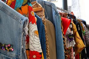 A variety of colorful and patterned garments hanging on a rack in a clothing store, showcasing different textures and styles, from denim to floral prints.