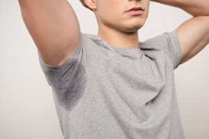 A person with a visible sweat stain on their gray t-shirt, lifting their arm.